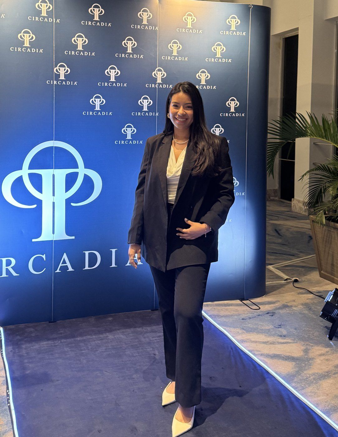 Ambar, con traje negro, frente al fondo con el logo de Circadia en un evento de la marca