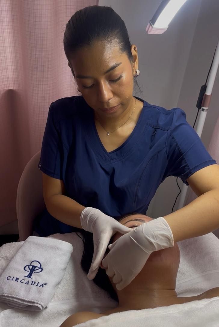 Ambar, con uniforme azul marino y guantes, trabaja con las manos sobre el rostro de una clienta en la camilla