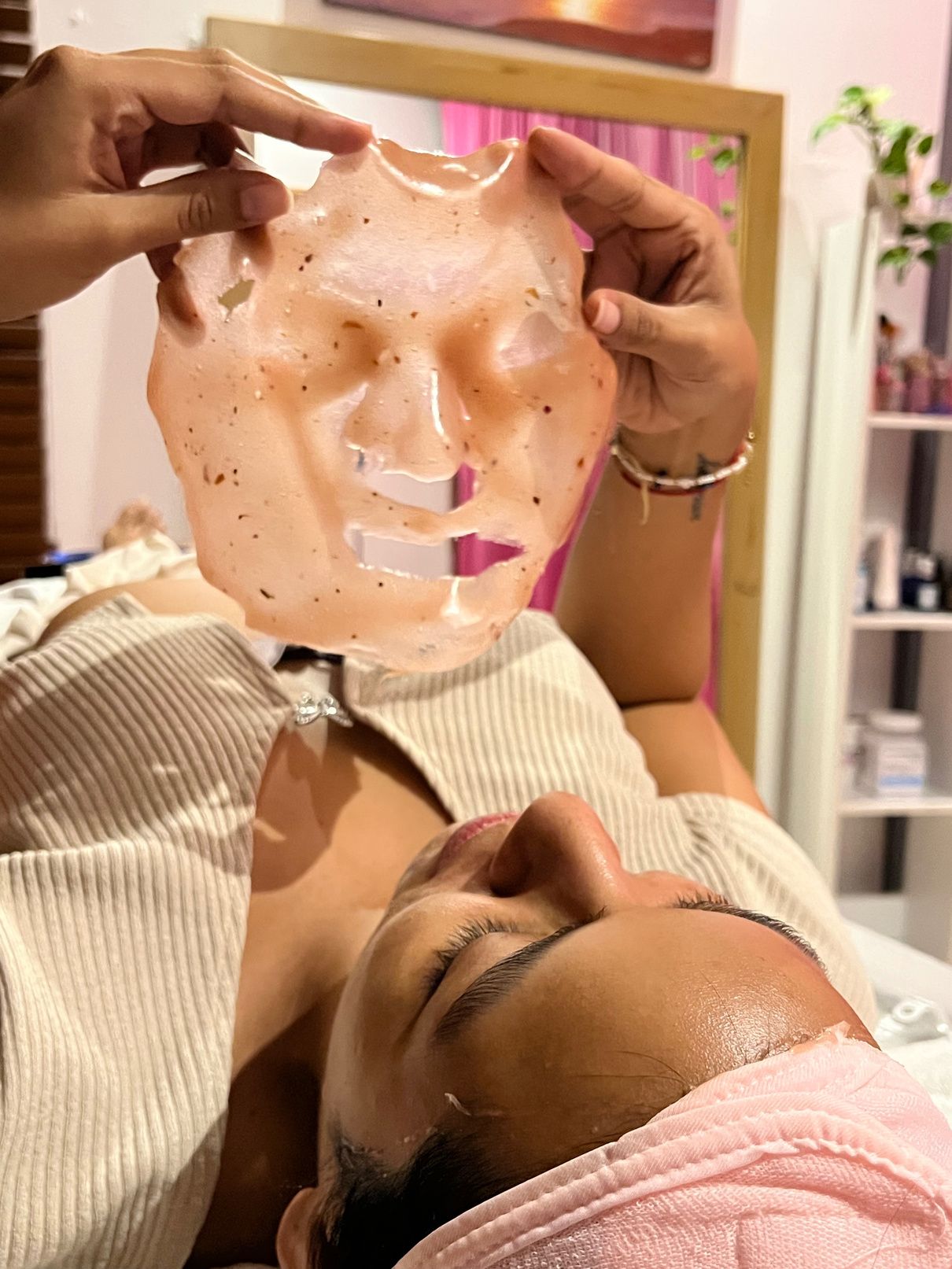 Retiro de una mascarilla hidratante del rostro de una clienta con banda rosada en la cabeza